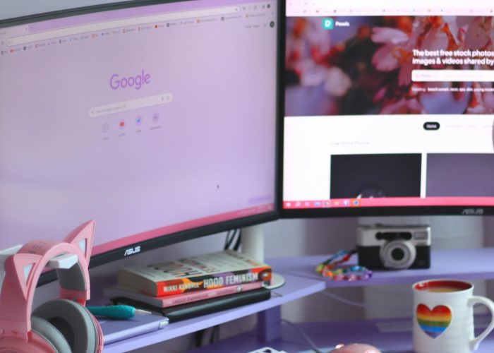 Stylish desk setup with dual monitors, keyboard, headphones, and cozy decor for tech enthusiasts.